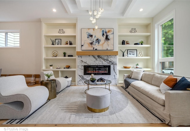 living room with built in features, plenty of natural light, an inviting chandelier, and a premium fireplace