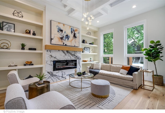 living room featuring coffered ceiling, beamed ceiling, a premium fireplace, light hardwood / wood-style floors, and built in shelves