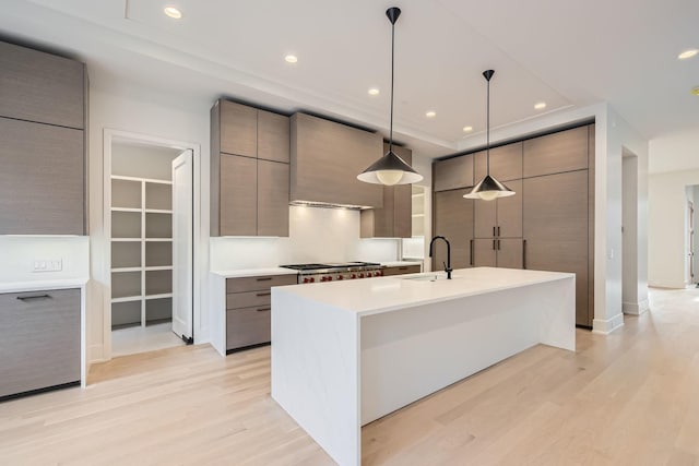 kitchen featuring decorative light fixtures, sink, a kitchen island with sink, light hardwood / wood-style floors, and wall chimney range hood