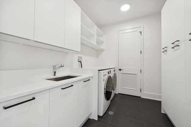 clothes washing area with dark tile patterned floors, sink, washing machine and clothes dryer, and cabinets