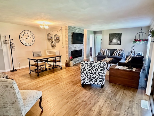 living room featuring a notable chandelier, a stone fireplace, and light hardwood / wood-style floors