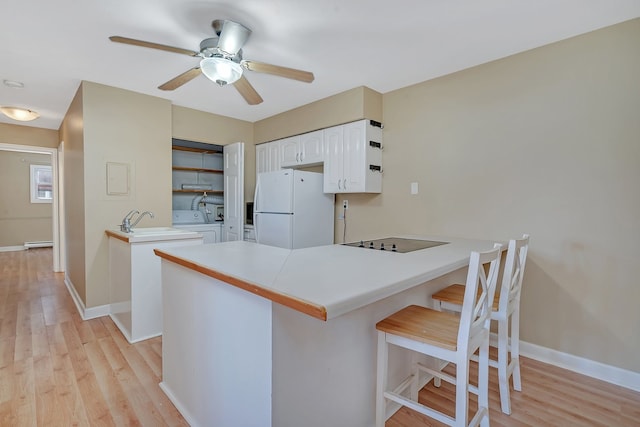 kitchen with white cabinets, white refrigerator, light hardwood / wood-style floors, kitchen peninsula, and a breakfast bar