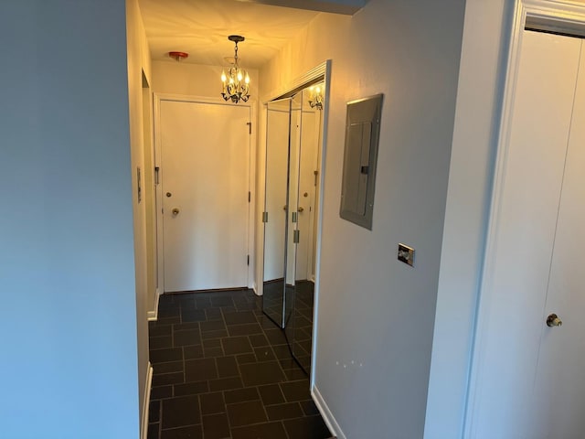 hall with dark tile patterned flooring, electric panel, and an inviting chandelier