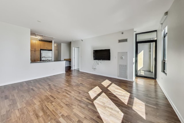 unfurnished living room with rail lighting, hardwood / wood-style flooring, and sink