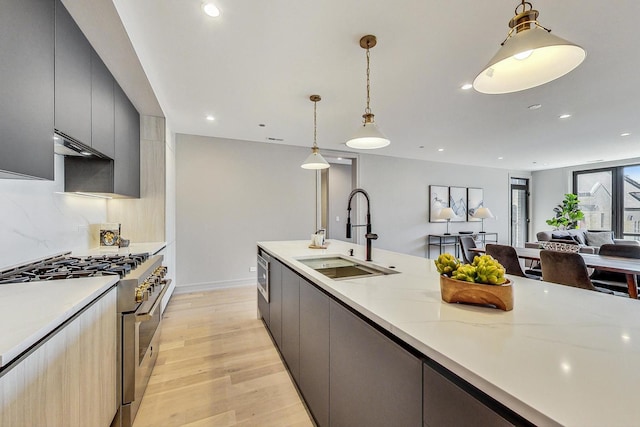 kitchen with light hardwood / wood-style flooring, stainless steel range, decorative light fixtures, light stone counters, and sink