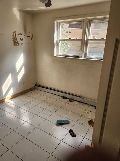 tiled spare room featuring a baseboard heating unit and ceiling fan