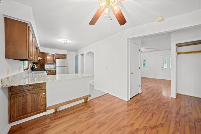 kitchen with stainless steel refrigerator, light hardwood / wood-style flooring, light stone counters, sink, and ceiling fan