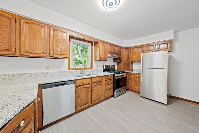 kitchen with appliances with stainless steel finishes, light stone countertops, light hardwood / wood-style floors, and sink