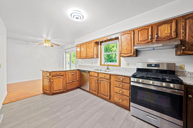 kitchen with light wood-type flooring, light stone counters, stainless steel appliances, and sink