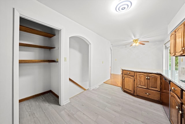 kitchen featuring stainless steel dishwasher, ceiling fan, light stone counters, and light wood-type flooring