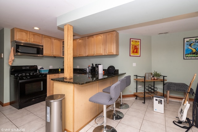 kitchen with black gas range oven, dark stone counters, light tile patterned floors, kitchen peninsula, and a breakfast bar area