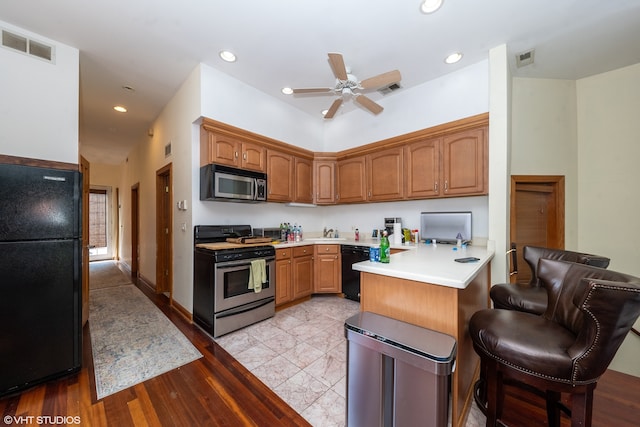 kitchen featuring light hardwood / wood-style flooring, black appliances, kitchen peninsula, ceiling fan, and a breakfast bar