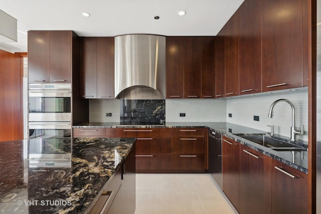 kitchen with stainless steel double oven, a sink, dark stone counters, wall chimney exhaust hood, and modern cabinets