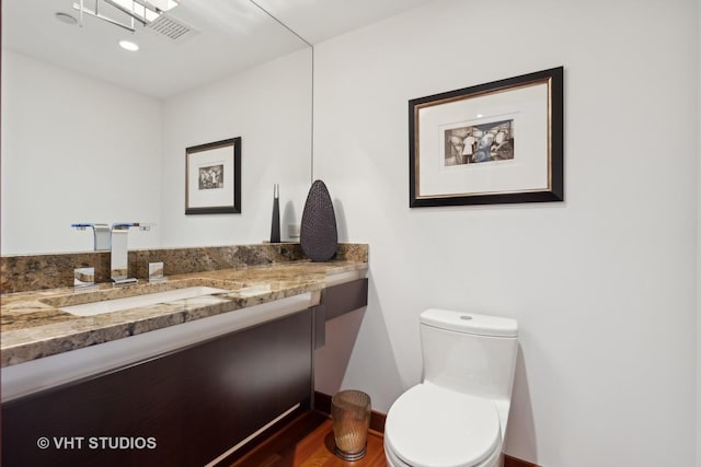 half bath with toilet, visible vents, wood finished floors, and vanity