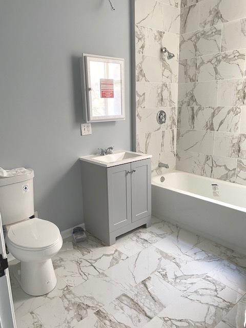 bathroom featuring toilet, marble finish floor,  shower combination, and vanity