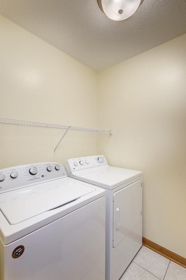 laundry area featuring washer and dryer, a textured ceiling, light tile patterned flooring, baseboards, and laundry area