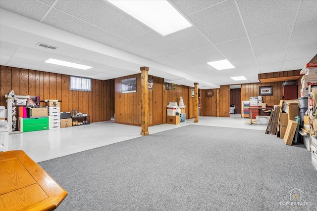 basement with carpet flooring, wooden walls, and a drop ceiling