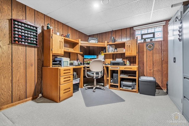 carpeted office featuring a paneled ceiling and wood walls