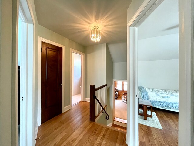 corridor featuring an inviting chandelier, lofted ceiling, and light wood-type flooring