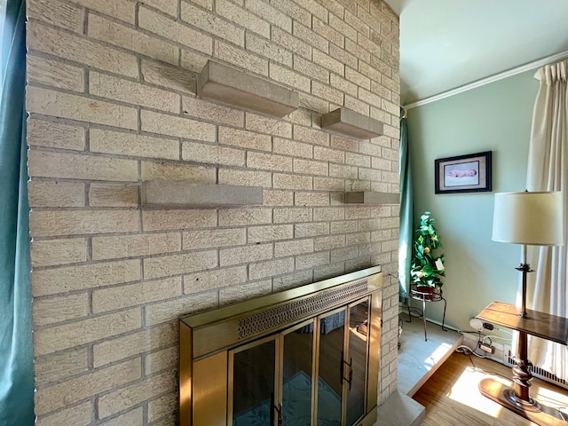 room details featuring ornamental molding, a brick fireplace, and wood-type flooring