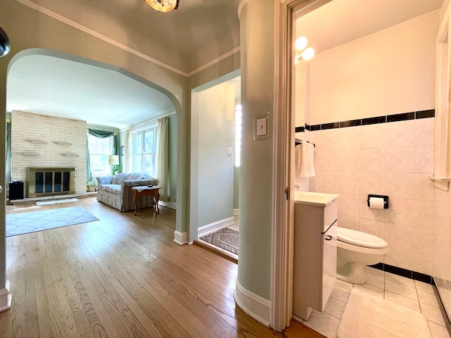 bathroom featuring tile walls, a brick fireplace, hardwood / wood-style flooring, and toilet