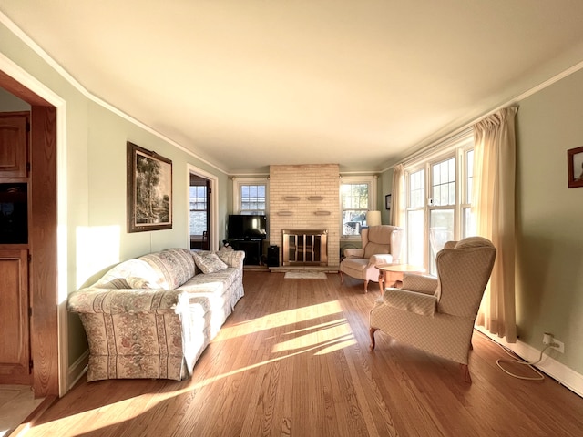 living room featuring ornamental molding, light hardwood / wood-style flooring, a brick fireplace, and plenty of natural light