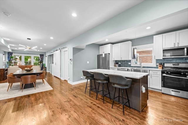 kitchen with backsplash, appliances with stainless steel finishes, white cabinetry, a kitchen breakfast bar, and a kitchen island