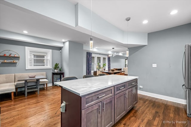 kitchen featuring dark hardwood / wood-style flooring, hanging light fixtures, a center island, light stone counters, and dark brown cabinetry