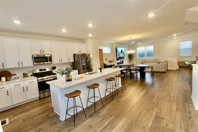 kitchen with white cabinets, stainless steel appliances, light hardwood / wood-style floors, a breakfast bar area, and a center island with sink