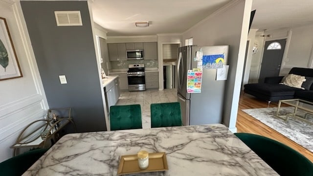 kitchen featuring gray cabinets, appliances with stainless steel finishes, ornamental molding, and light hardwood / wood-style floors