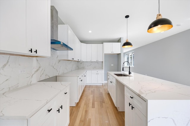 kitchen with light stone countertops, wall chimney exhaust hood, pendant lighting, an island with sink, and sink