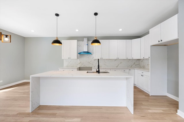 kitchen with backsplash, wall chimney range hood, an island with sink, sink, and light hardwood / wood-style floors