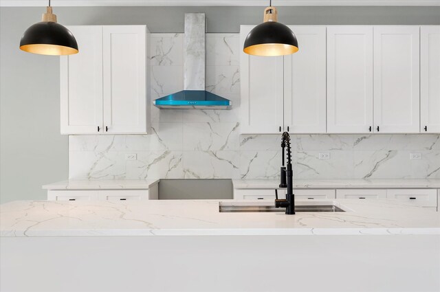 kitchen with hanging light fixtures, light stone countertops, wall chimney exhaust hood, and white cabinetry