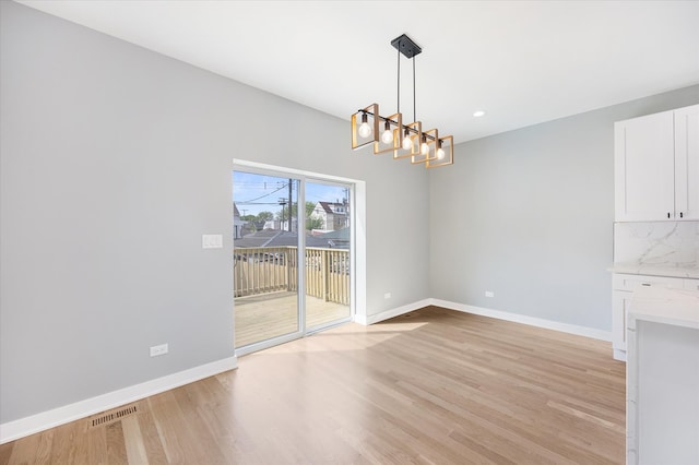 unfurnished dining area with light wood-type flooring and a notable chandelier