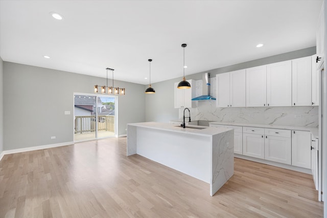 kitchen with a kitchen island with sink, white cabinetry, decorative backsplash, and wall chimney range hood