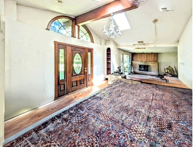 entrance foyer with wood-type flooring, a chandelier, vaulted ceiling with beams, and a fireplace