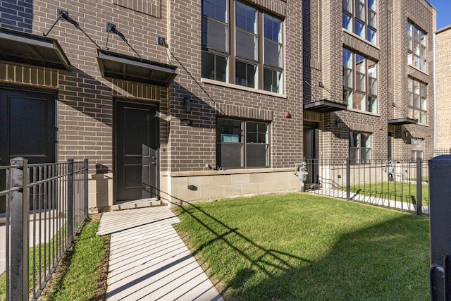 view of exterior entry featuring a yard, brick siding, and fence