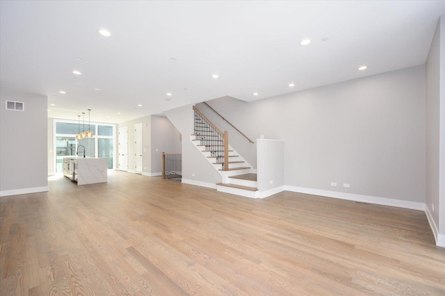 unfurnished living room featuring light wood-type flooring, stairway, visible vents, and recessed lighting