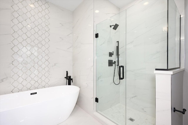 bathroom featuring marble finish floor, a soaking tub, a marble finish shower, and tile walls