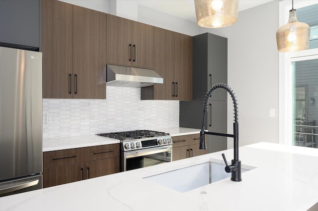 kitchen with appliances with stainless steel finishes, a sink, under cabinet range hood, pendant lighting, and backsplash