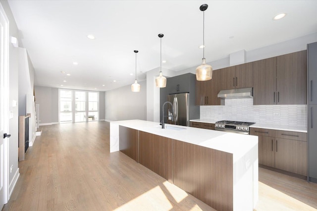 kitchen with stainless steel appliances, light countertops, decorative backsplash, a sink, and under cabinet range hood