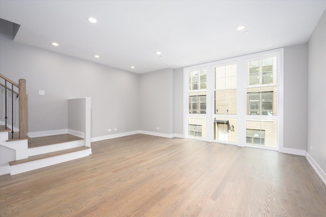 unfurnished living room featuring baseboards, stairway, recessed lighting, and light wood-style floors