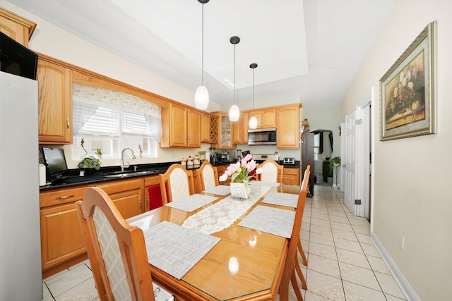 kitchen featuring a sink, a tray ceiling, stainless steel microwave, freestanding refrigerator, and light tile patterned flooring