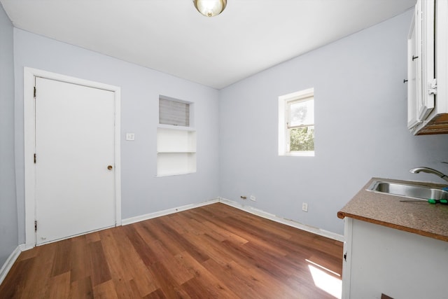 unfurnished dining area featuring a sink, baseboards, built in shelves, and wood finished floors