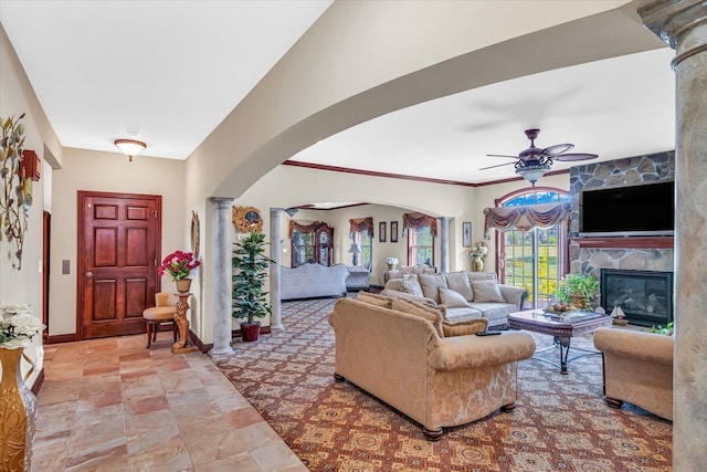 living room with ceiling fan, a stone fireplace, and decorative columns