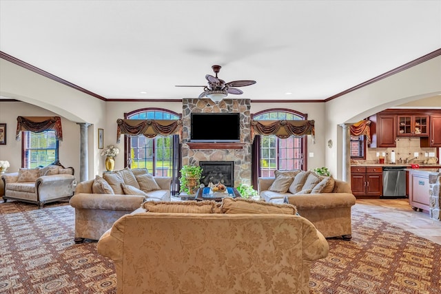 living room with ornamental molding, bar, ceiling fan, and a stone fireplace