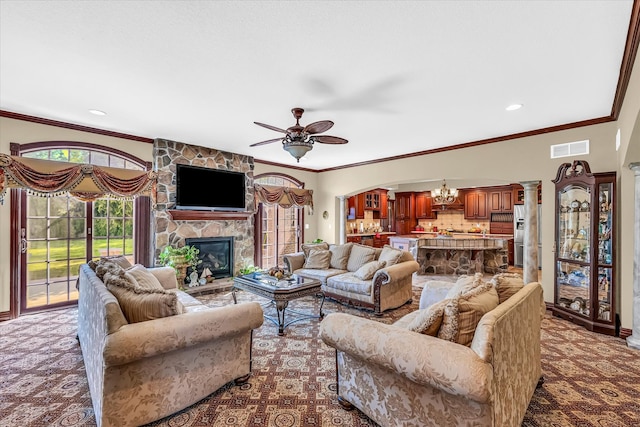 carpeted living room featuring ornamental molding, ceiling fan with notable chandelier, and a stone fireplace