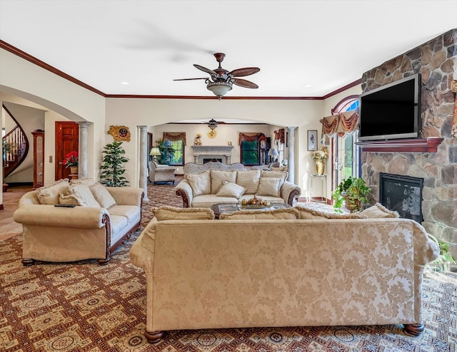 carpeted living room with ceiling fan, ornamental molding, and a stone fireplace