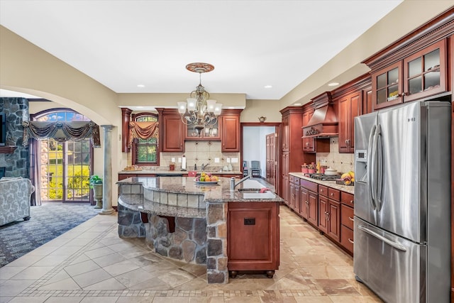 kitchen with appliances with stainless steel finishes, light stone counters, custom exhaust hood, a notable chandelier, and tasteful backsplash