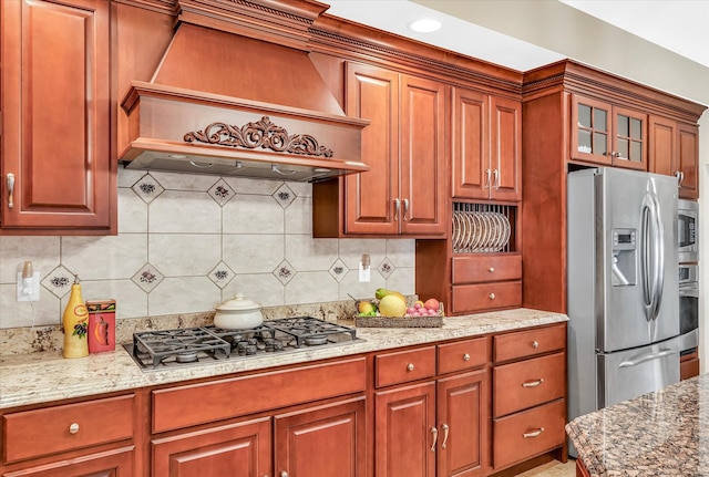 kitchen featuring appliances with stainless steel finishes, light stone counters, decorative backsplash, and custom range hood